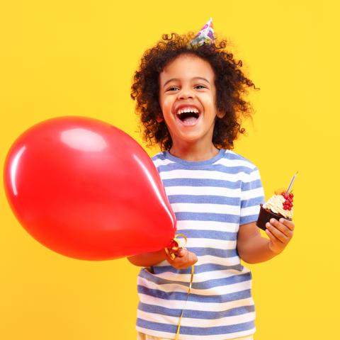 Young boy holding balloon and cupcake