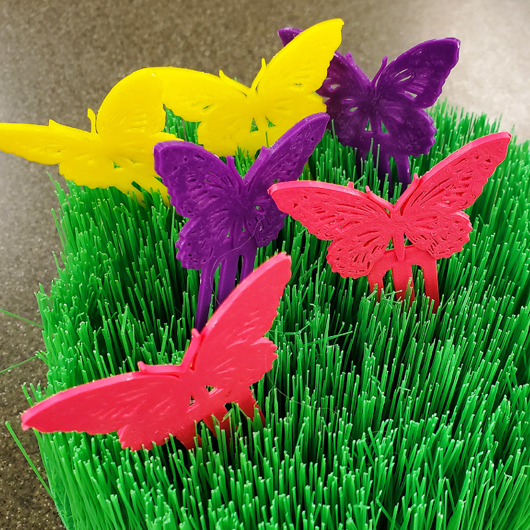 Pink, yellow, and purple 3D printed butterflies in 3D printed grass