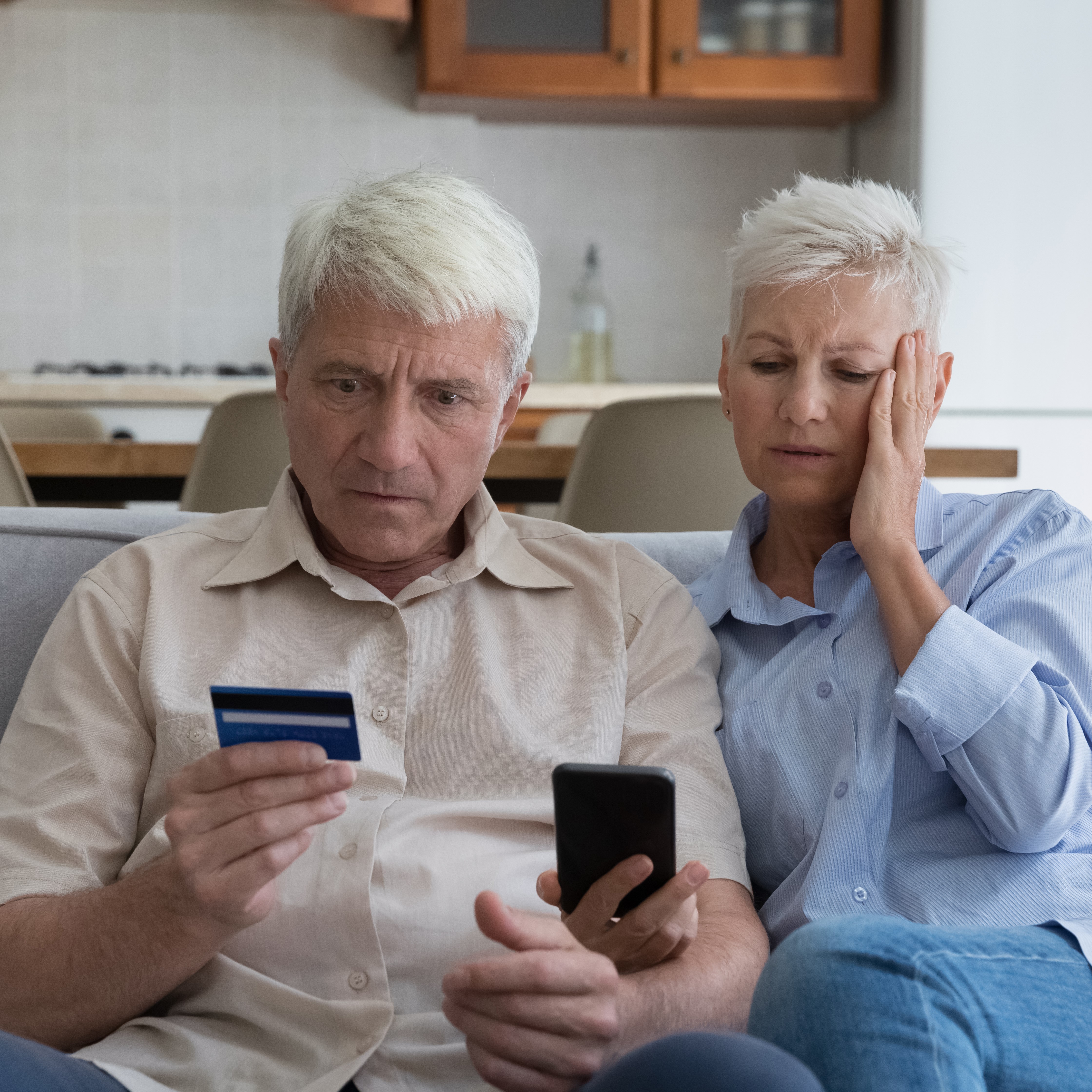 Senior couple looking upset holding credit card and cellphone