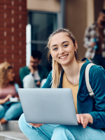 Student sitting on outdoor steps with laptop smiling to camera