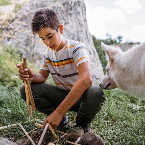Teen building a fire in the woods with their dog