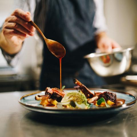 Cook adding sauce to food on plate