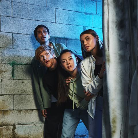 Four teens looking out behind wall