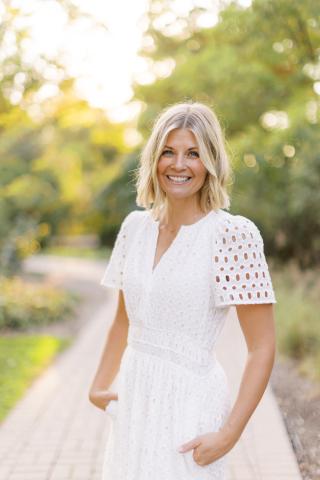 presenter, Jess Trayser, standing outside in a white dress, facing and smiling at the camera