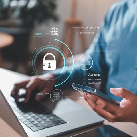 Someone on laptop holding cellphone with security icon over image