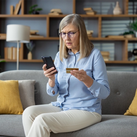 Woman appearing anxious looking at cellphone and credit card