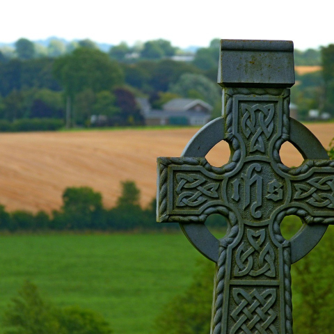 stone celtic cross with green landscape in background