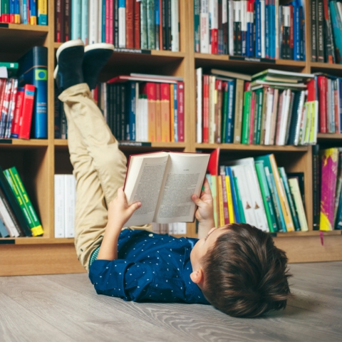 Boy reading on floor with legs resting on bookshelf
