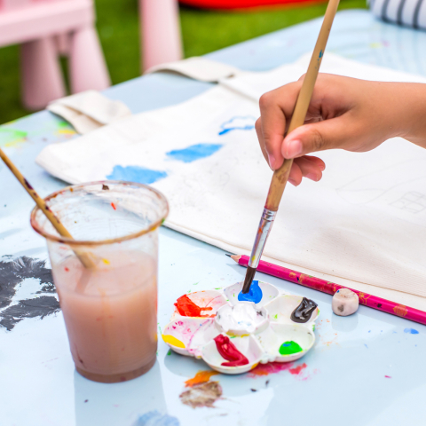 hand holding paint brush painting canvas tote bag