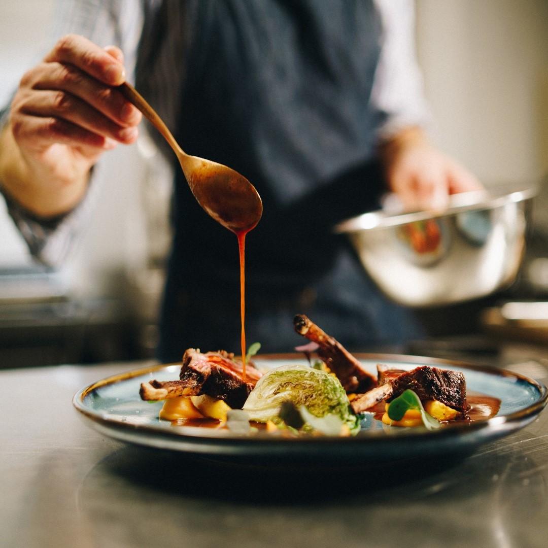 Cook adding sauce to food on plate
