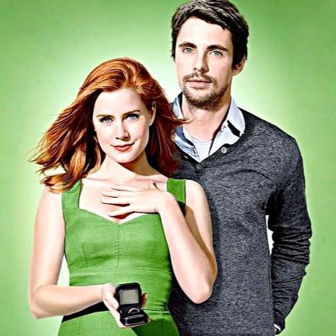 Woman holding an engagement ring with man standing behind