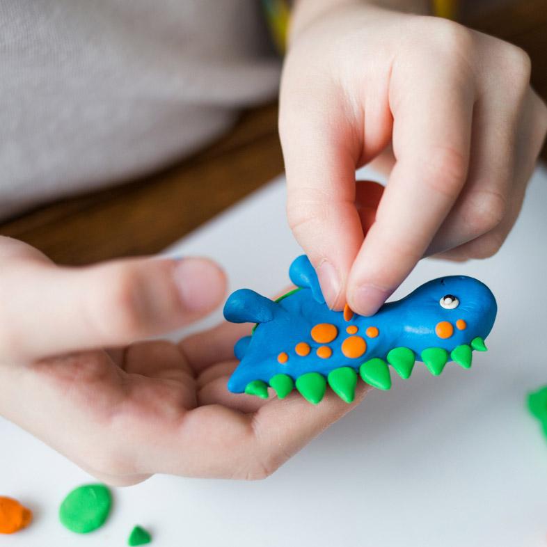 Hands holding clay dinosaur
