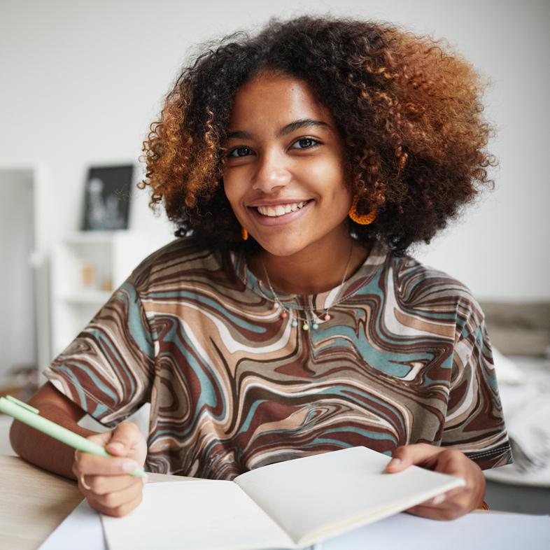 teen writing in notebook smiling