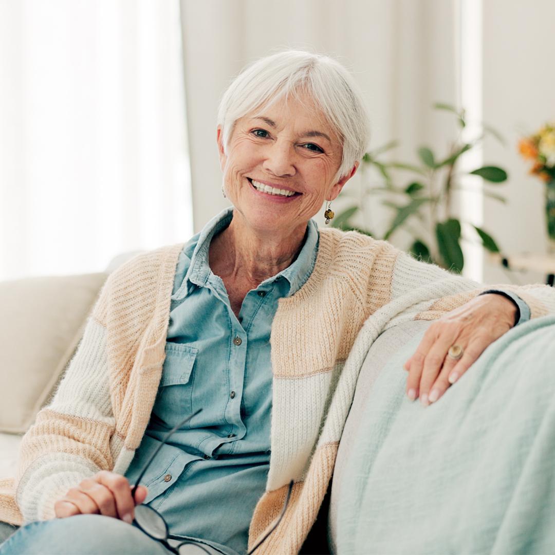 Senior woman sitting on couch smiling at camera