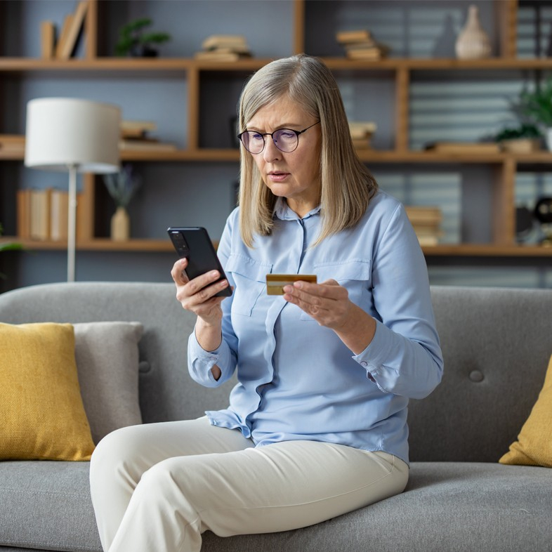 Woman appearing anxious looking at cellphone and credit card