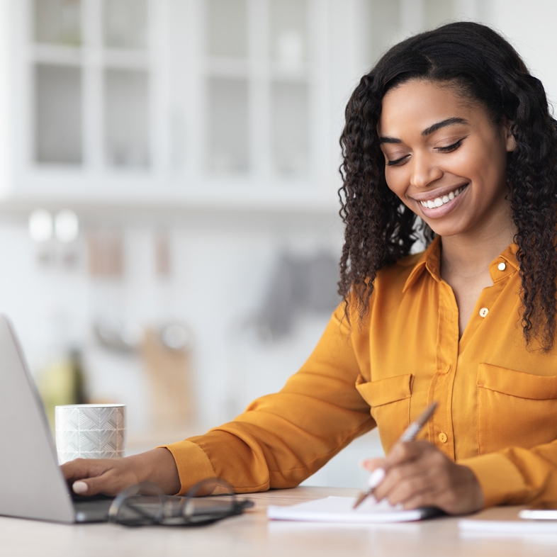 Woman on computer smiling while writing a note