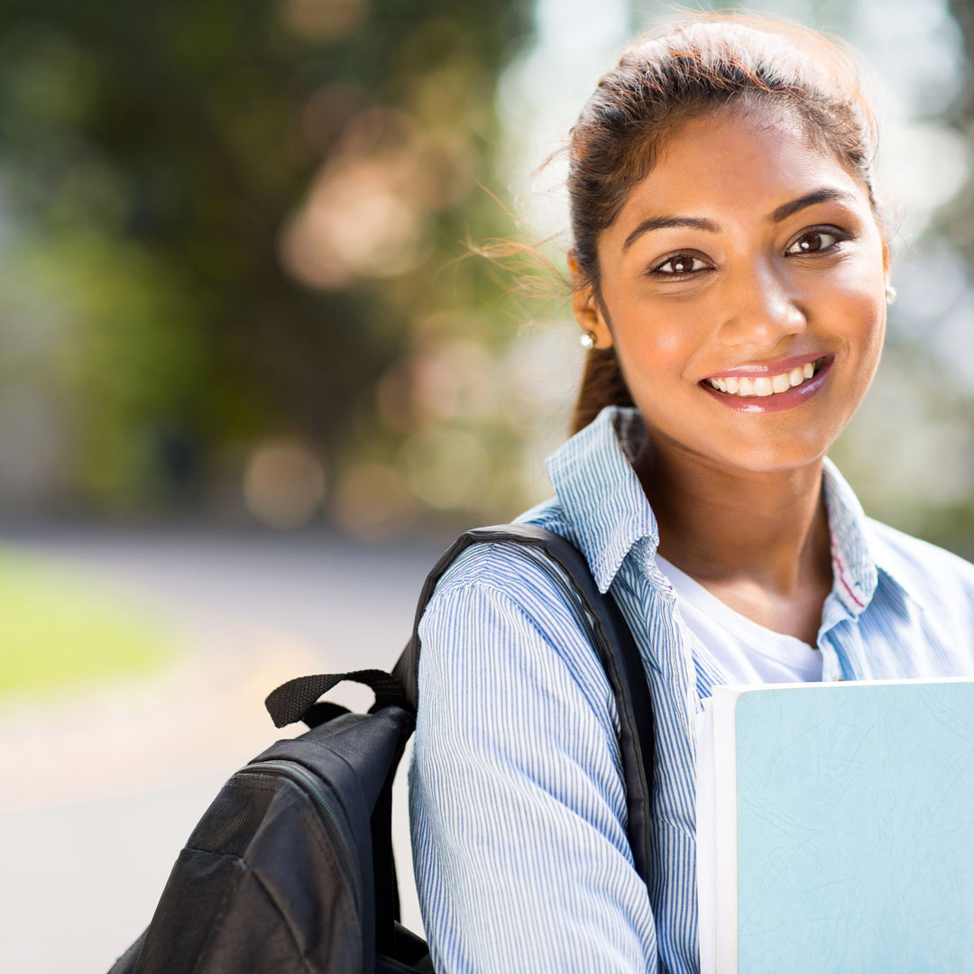 Teen smiling wearing backpack and carrying textbook