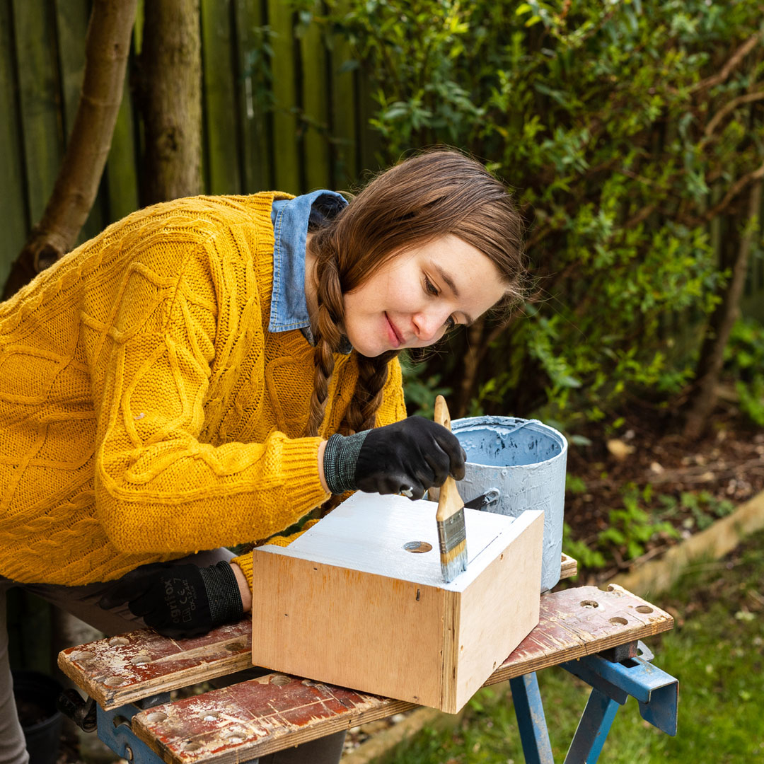 Teen girl painting a birdhouse outside