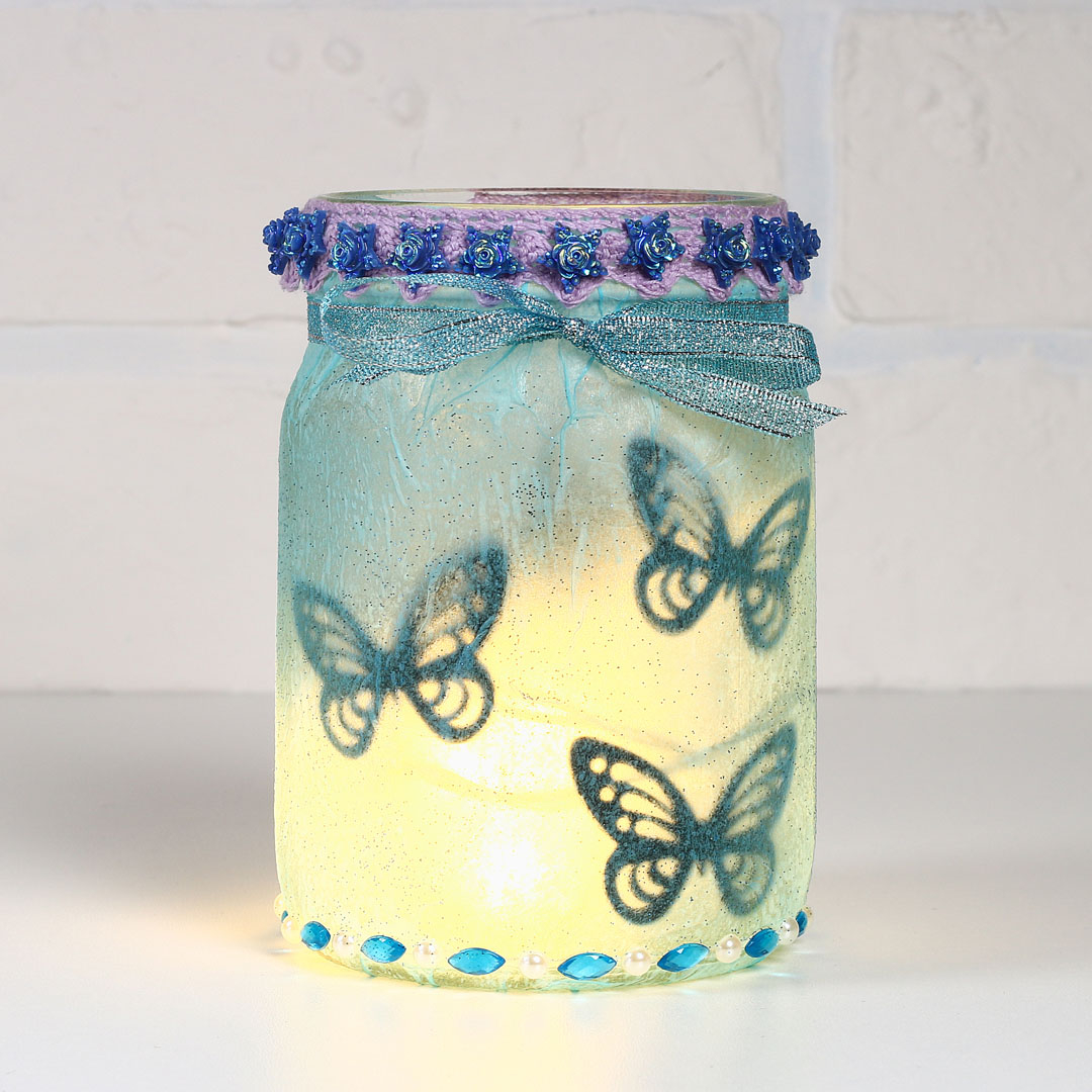 Mason jar lantern decorated with glitter, butterflies, and ribbon