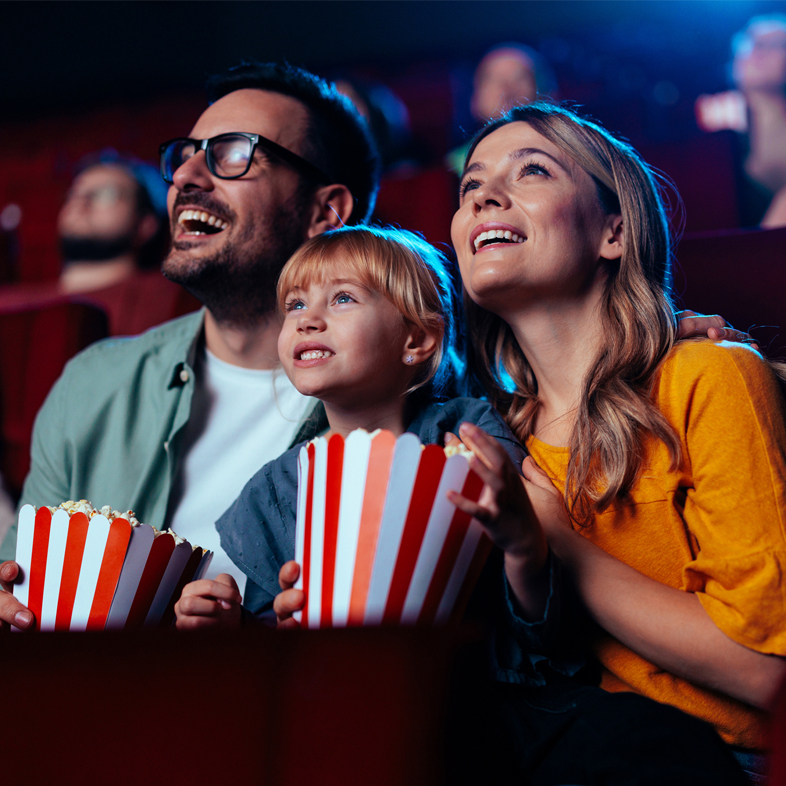 Parents with child looking up at movie screen holding popcorn.
